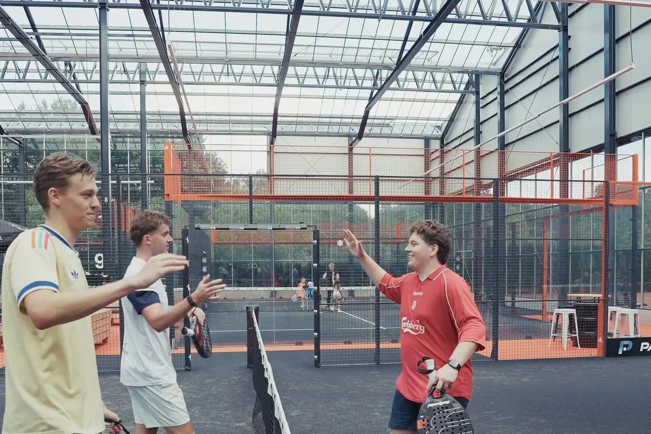 Vier spelers geven elkaar een hand bij het net in de hal op Reyerparc, onder het glazen dak